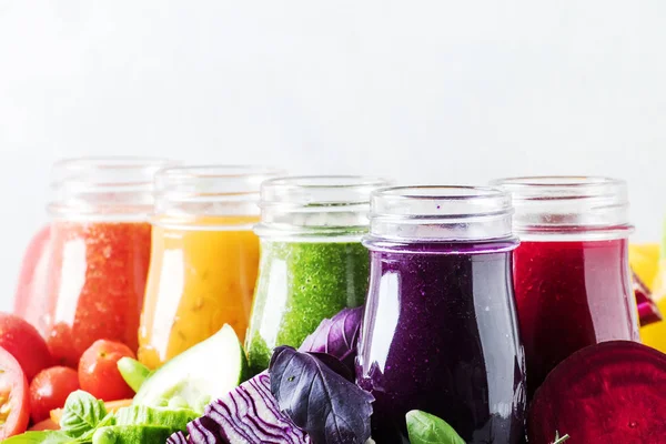 Multicolored vegan vegetable juices and smoothies in glass bottles on gray table, selective focus