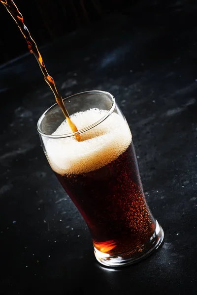 Dark english beer, ale or stout is poured into glass, dark bar counter, space for text, selective focus