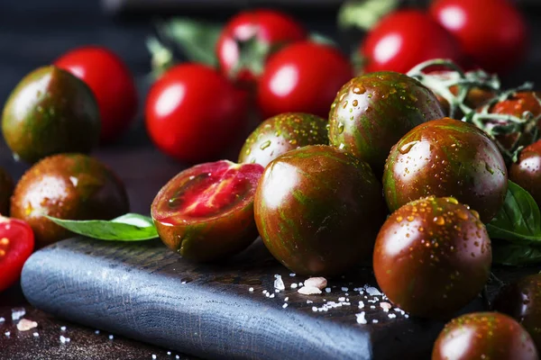 Brown cherry tomatoes with sea salt and green basil on dark table, autumn harvest, selective focus