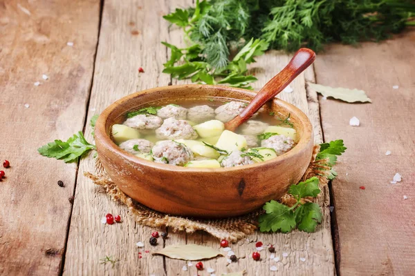 Homemade soup with turkey meatballs, potatoes and parsley in wooden bowl, rustic style, selective focus