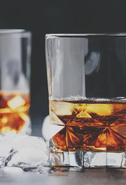 Bourbon with ice in glasses on gray bar counter, selective focus