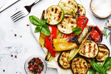 Grilled colorful vegetables, aubergines, zucchini, pepper with spice and green basil on serving board on white background, top view clipart