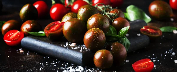 Brown cherry tomatoes with sea salt and green basil on dark table, autumn harvest, selective focus