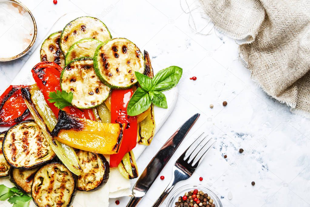 Grilled colorful vegetables, aubergines, zucchini, pepper with spice and green basil on serving board on white background, top view