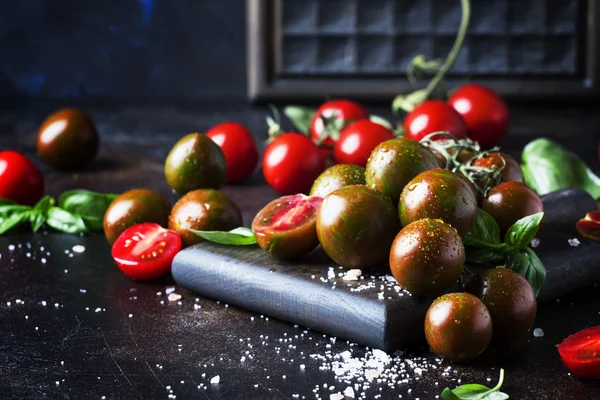 Brown cherry tomatoes with sea salt and green basil on dark table, autumn harvest, selective focus