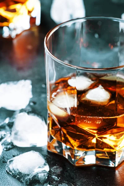 Bourbon with ice in glasses on gray bar counter, selective focus