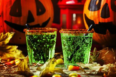 Cadılar Bayramı kompozisyon şenlikli yeşil İçecek ve içme pumpkins, tatlı Mısır, saman ve düşmüş ile gülümseyen koyu arka plan üzerinde seçici odak bırakır