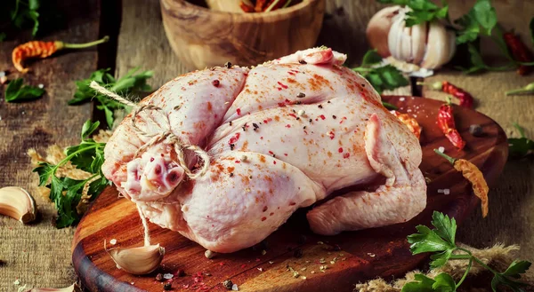 Raw whole chicken with spices and marinade, old wooden table, still life, rustic style, top view