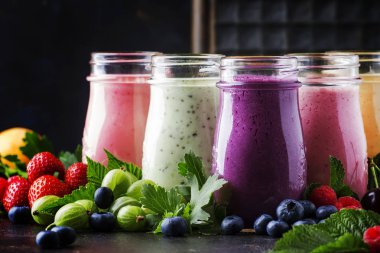 Sağlıklı ve kullanışlı renkli berry kokteyller, smoothies ve yoğurt, taze meyve ve çilek kahverengi tablo, seçici odak milkshakes