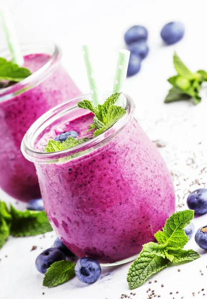 Purple homemade yogurt or smoothie with blueberries, chia seeds and mint leaves in glass jars on gray background, selective focus