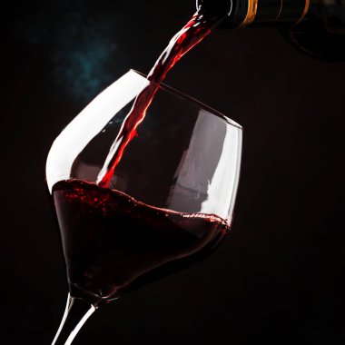 Red wine from grapes of pinot noir varieties poured into large wine glass, wine tasting, on dark background, low key, selective focus clipart