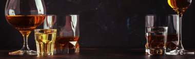 Set of strong alcoholic drinks in glasses and shot glass in assortment: vodka, rum, cognac, tequila, brandy and whiskey. Dark vintage background, banner, selective focus clipart
