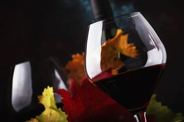 干燥的红葡萄酒从黑皮诺葡萄在大杯子 秋天仍然生活与红色和黄色叶子在黑暗的背景 选择性焦点 — 图库照片