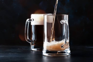 Alman light bira iki bardak, kupa, counter arka plan, karanlık içine seçici odak bira dökülür
