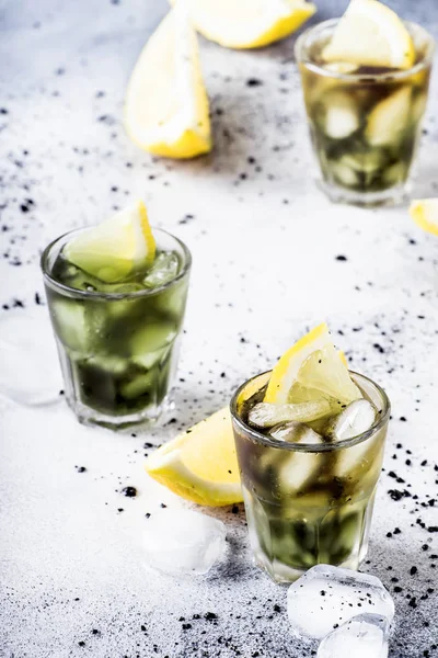 Healthy food and drink concept: iced black detox mineral water with crushed ice and lemon slices in glasses, activated charcoal, gray background, trendy beverage, selective focus