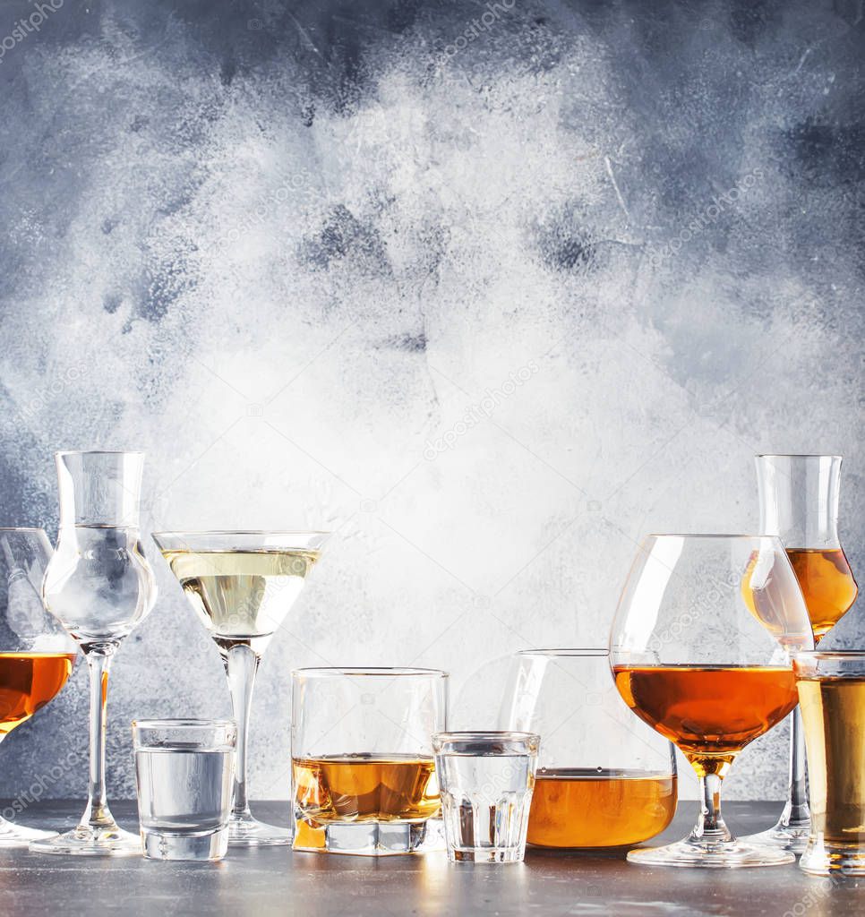 Selection of hard strong alcoholic drinks in big glasses and small shot glass in assortent: vodka, cognac, tequila, brandy and whiskey, grappa, liqueur, vermouth, tincture, rum. Gray bar counter background, selective focus, copy space