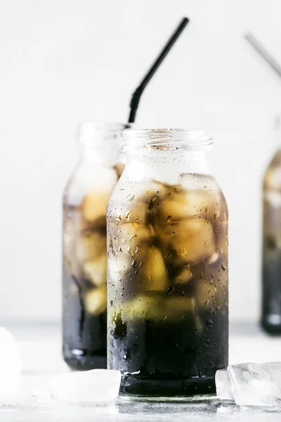 Healthy food and drink concept: cold black detox mineral water with crushed ice in glass bottles, with activated charcoal, gray stone table background, trendy beverage, copy space, selective focus