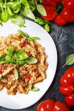 Beyaz tabak, koyu arka plan mutfak masası, üstten görünüm yeşil fesleğen ile kıyılmış et ve domates soslu lezzetli makarna