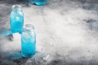 Sport and fitness drink concept, very cold refreshing isotonic blue water in bottles, gray table background, selective focus clipart