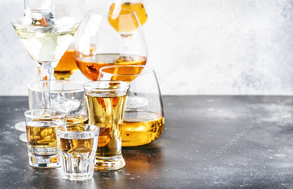 Selection of hard strong alcoholic drinks  and spirits in big glasses and small shot glass in assortment: vodka, cognac, tequila, brandy and whiskey, grappa, liqueur, vermouth, tincture, rum. Gray bar counter background, selective focus, copy space