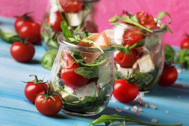 Yaz salatası roka, yumuşak peynir, domates ve prosciutto cam kavanozlar, trendy pembe mavi arka plan, seçici odak