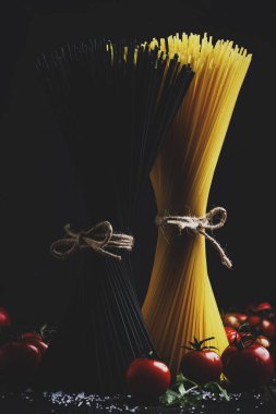 Siyah ve sarı makarna spagetti, iple bağlı, dikey olarak karanlık mutfak masasında ingridients ile düşük anahtar natürmort, seçici odak yemek için hazır
