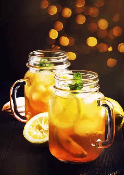 Black ice tea with lemon slice in glass jar on dark kitchen table background, summer cool soft drink, selective focus