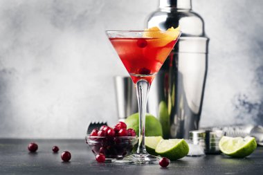 Classic alcoholic cocktail cosmopolitan with vodka, liqueur, cranberry juice, lime, ice and orange zest, gray bar counter background, bartender tols, space for text clipart