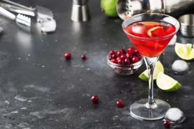 Classic alcoholic cocktail cosmopolitan with vodka, liqueur, cranberry juice, lime, ice and orange zest, gray bar counter background, bartender tols, space for text clipart