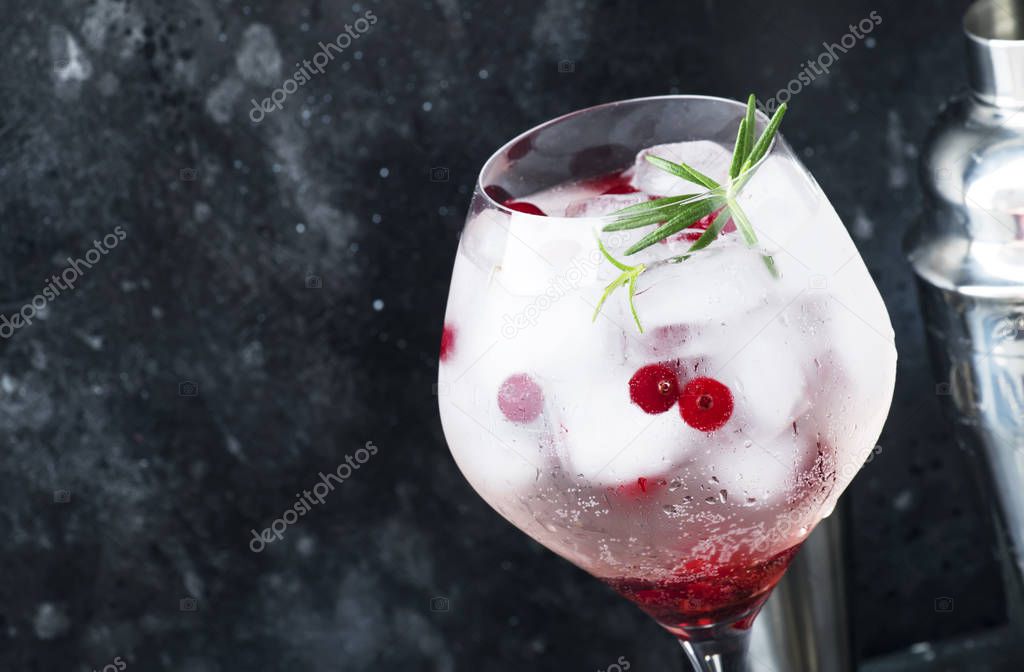 Cranberry cocktail with ice, rosemary and berries in big wine glass, bar tools, gray bar counter background, top view