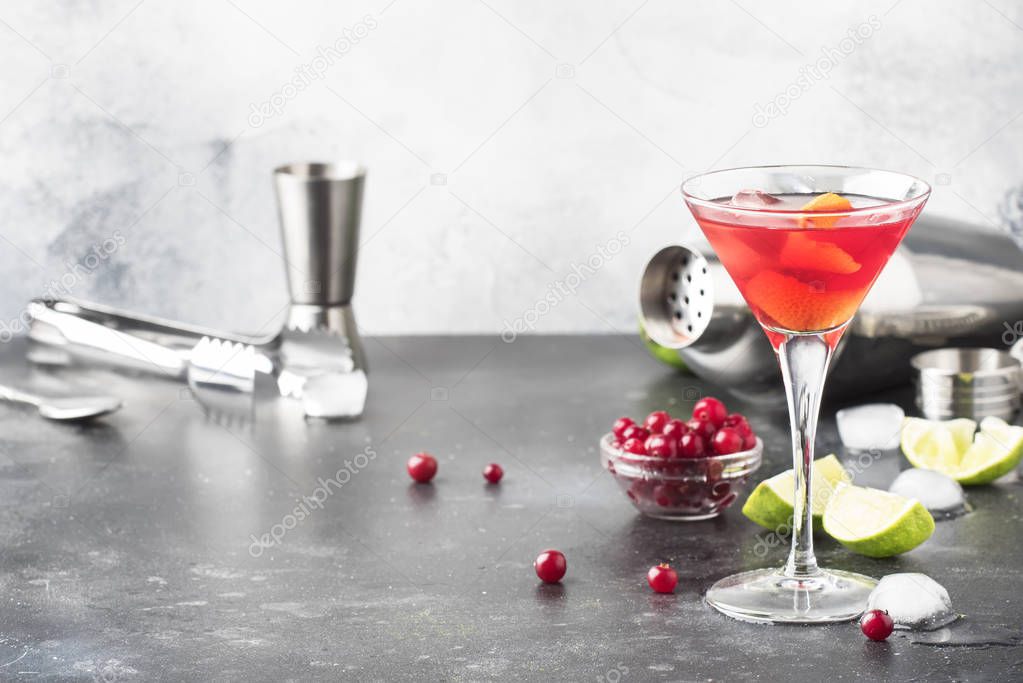 Classic alcoholic cocktail cosmopolitan with vodka, liqueur, cranberry juice, lime, ice and orange zest, gray bar counter background, bartender tols, space for text