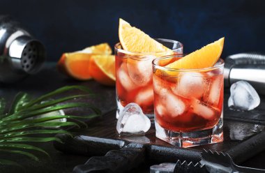 Yaz kuru cin, kırmızı vermut ve kırmızı acı, portakal dilimi ve buz küpleri ile alkollü kokteyl Negroni. Brown bar counter arka plan, araçları, metin, seçici odak için yer