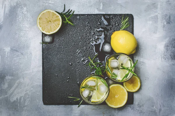 Summer fizzy cocktail with lemon, rosemary and ice, gray table background, toned image, top view