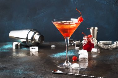 Klasik alkollü Manhattan kokteyli. Amerikan viskisi, kırmızı vermut, acı, buzlu ve vişneli martini bardağı, gece mavisi kahverengi arka plan, bar aletleri, kopyalama alanı, seçici odak noktası.