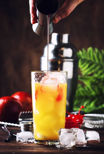 Summer tequila sunrise cocktail with silver tequila, grenadine syrup, orange and ice cubes. Wooden bar counter in the beach bar. Bartender preparing cocktail. Selective focus. Place for text