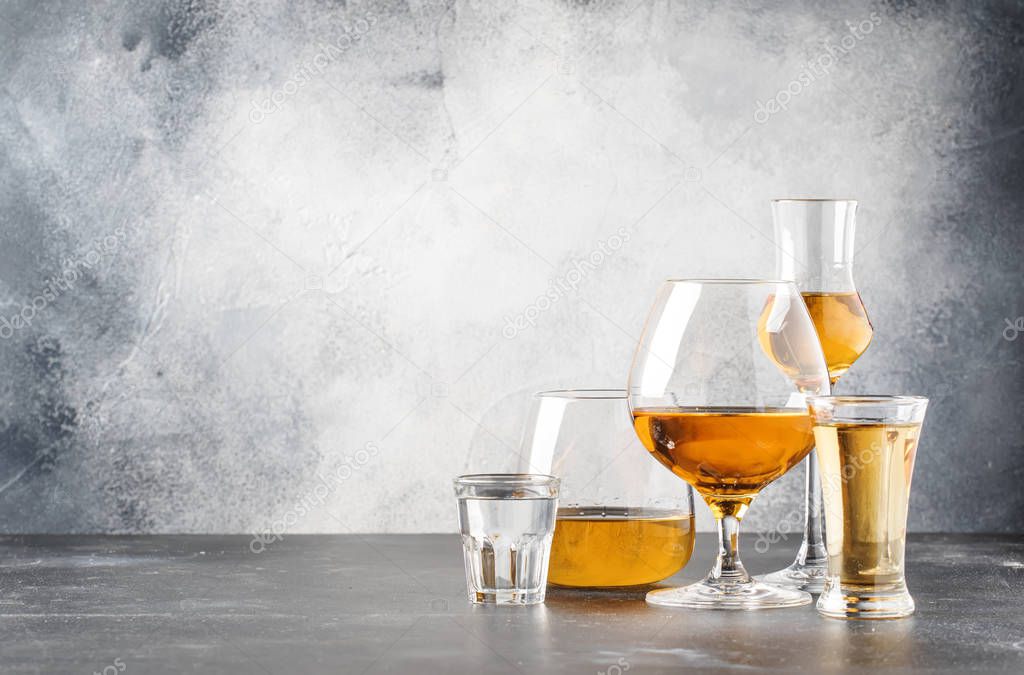 Set of hard strong alcoholic drinks and spirits in glasses in assortment: vodka, cognac, tequila, brandy and whiskey, grappa, liqueur, vermouth, tincture, rum. Gray bar counter background, selective focus, copy space