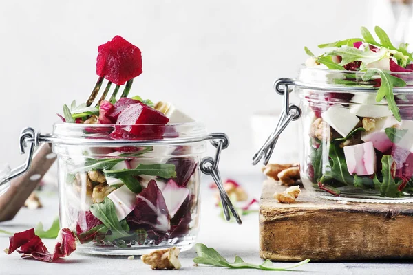 Beet salad with arugula, goat cheese and nuts, trendy salad jar, gray kitchen table background, selective focus