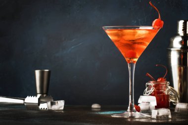 Klasik alkollü Manhattan kokteyli. Amerikan viskisi, kırmızı vermut, acı, buzlu ve vişneli martini bardağı, gece mavisi kahverengi arka plan, bar aletleri, kopyalama alanı, seçici odak noktası.