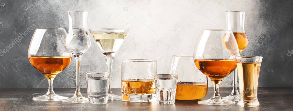 Set of hard strong alcoholic drinks and spirits in glasses in assortment: vodka, cognac, tequila, brandy and whiskey, grappa, liqueur, vermouth, tincture, rum. Gray bar counter background, selective focus, copy space, banner