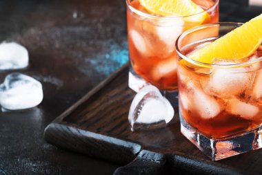Sek cin, kırmızı vermut, kırmızı acı, portakal dilimi ve buz küplü Negroni kokteyli. Kahverengi bar tezgahı arka planı, bar araçları, gece havası, kopyalama alanı, seçici odak