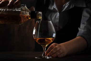 Barmen büyük şarap cam eski konyak veya brendi dökülen bar sayacı. Antika ahşap arka plan pub veya bar, gece ruh hali. Tonlama, seçici odak metin için yer