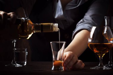 Barmen eski bar sayacı üzerinde küçük çekim cam altın tekila döker. Pub veya barda vintage ahşap arka plan, gece ruh hali. Metin, tonlama, seçici odaklama için yer