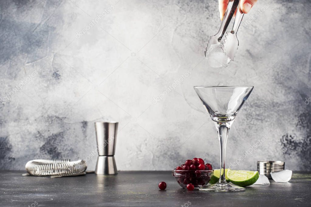 Preparation cosmpolitan cocktail with vodka, liqueur, cranberry juice, lime, ice and orange zest, gray bar counter background, copy space