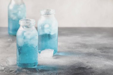 Summer refreshing cold drink, isotonic blue water in bottles, gray table background, selective focus clipart