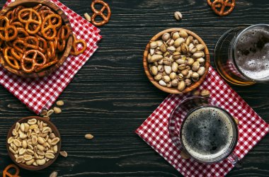 Bardaklarda hafif ve koyu bira ve tuzlu atıştırmalıklar ve fındıklar, koyu ahşap masa, fotokopi alanı olan çerçeve, üst görünüm