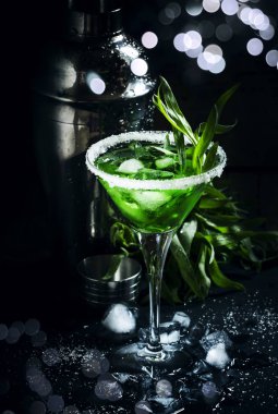 Shaker, seçici odak ile koyu arka plan üzerinde martini cam tarhun ve buz ile yeşil kokteyl 