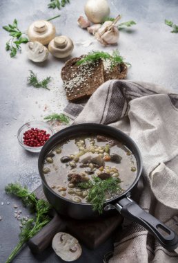 Sığır eti ve kepekli arpa ile sıcak etli sebze mantar çorbası. Siyah ekmek ile, metal tavada, üst görünüm, gri mutfak masası, kopya alanı