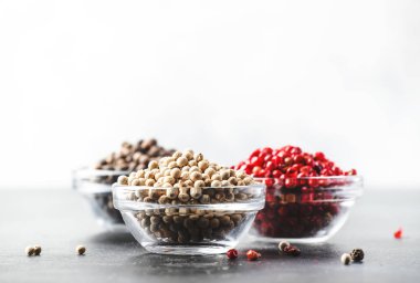 Kaselerde siyah, beyaz ve pembe gül biber, gri mutfak masasında çeşitli baharatlar, seçici odak