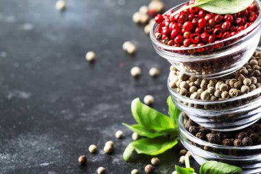 Kaselerde siyah, beyaz ve pembe gül biber, gri mutfak masasında çeşitli baharatlar, seçici odak