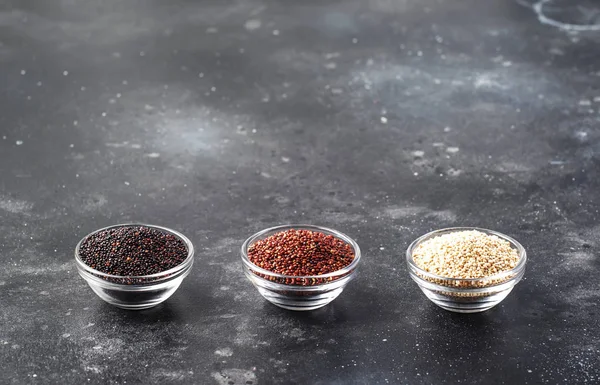 Black, white and red quinoa in bowls, raw quinoa groats assorted, gray kitchen table, selective focus